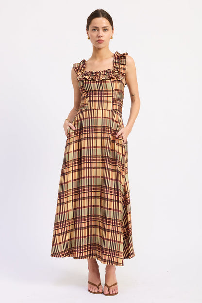A woman modeling a sleeveless maxi dress with a ruffled neckline and a plaid pattern in beige, brown, and red, standing against a plain white studio background.