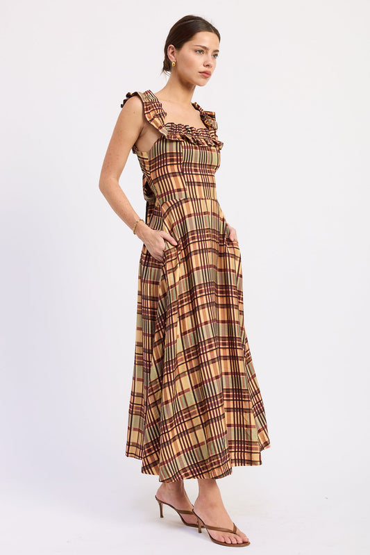 A woman modeling a sleeveless plaid maxi dress with ruffled shoulder straps and side pockets, paired with brown heeled sandals, against a plain white studio background.