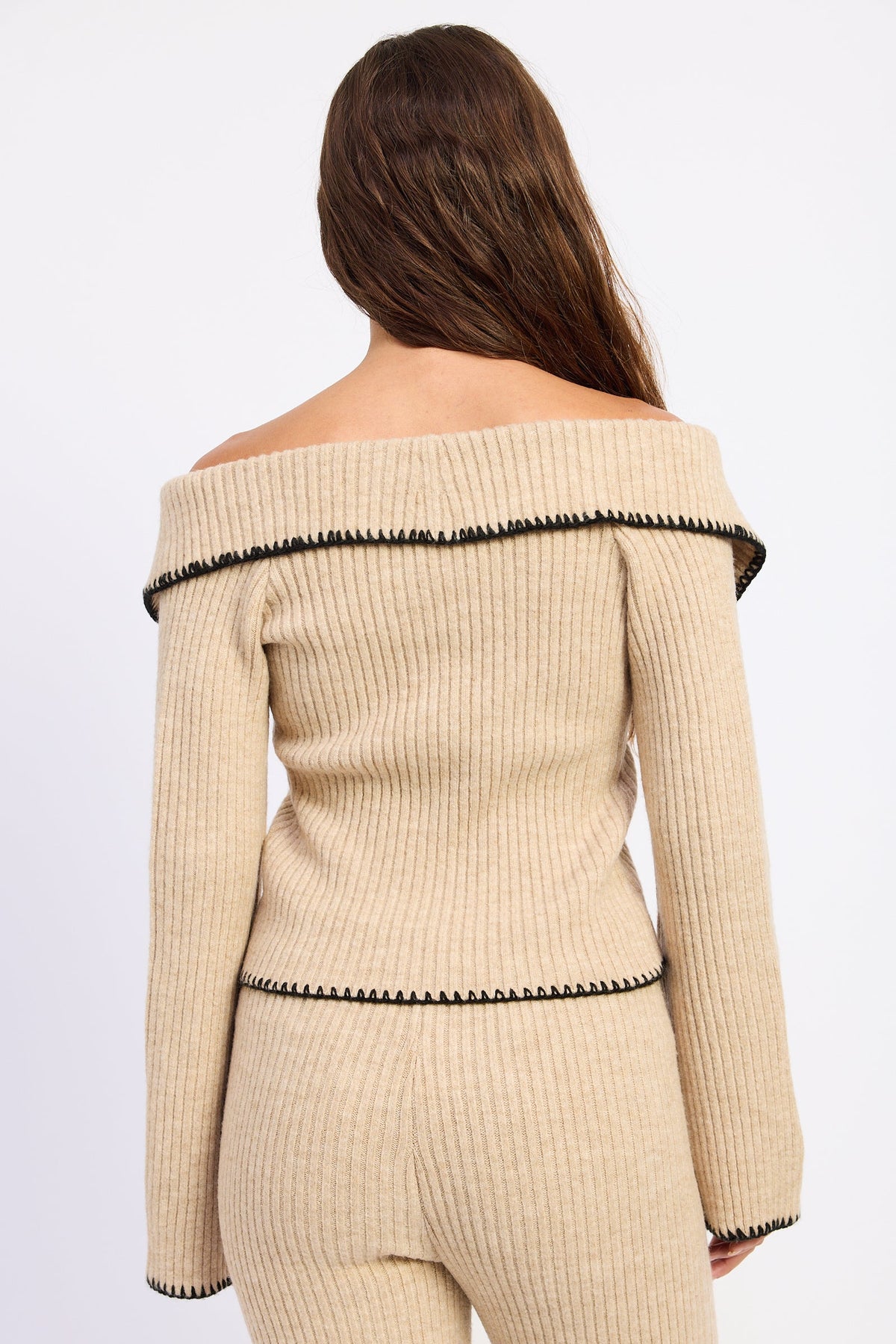 A woman shown from the back wearing a beige ribbed knit off-the-shoulder sweater and matching pants with black trim details, against a plain white studio background.