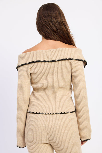 A woman shown from the back wearing a beige ribbed knit off-the-shoulder sweater and matching pants with black trim details, against a plain white studio background.