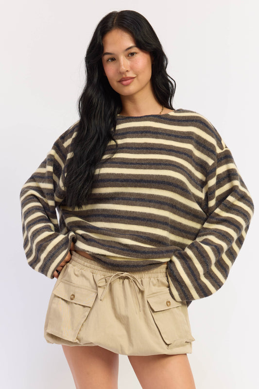 A woman modeling a fuzzy long-sleeve knit sweater with horizontal dark brown and beige stripes, paired with khaki cargo shorts, against a plain light gray background.