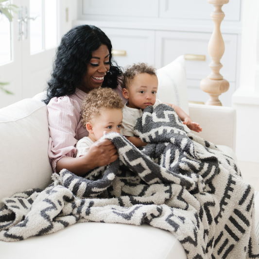 Woman sitting on a couch with two children under a DOUBLE-LAYER BAMBONI® XL BLANKET in a bright room.