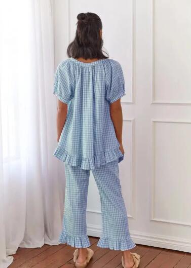 Person wearing a blue checkered outfit standing in a room with white walls and wooden floor.