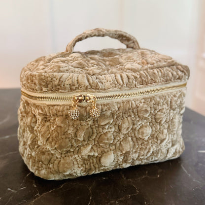 Beige textured jewelry box with gold zipper on a dark surface