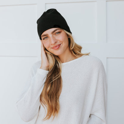 Woman wearing a black beanie and white sweater against a white background