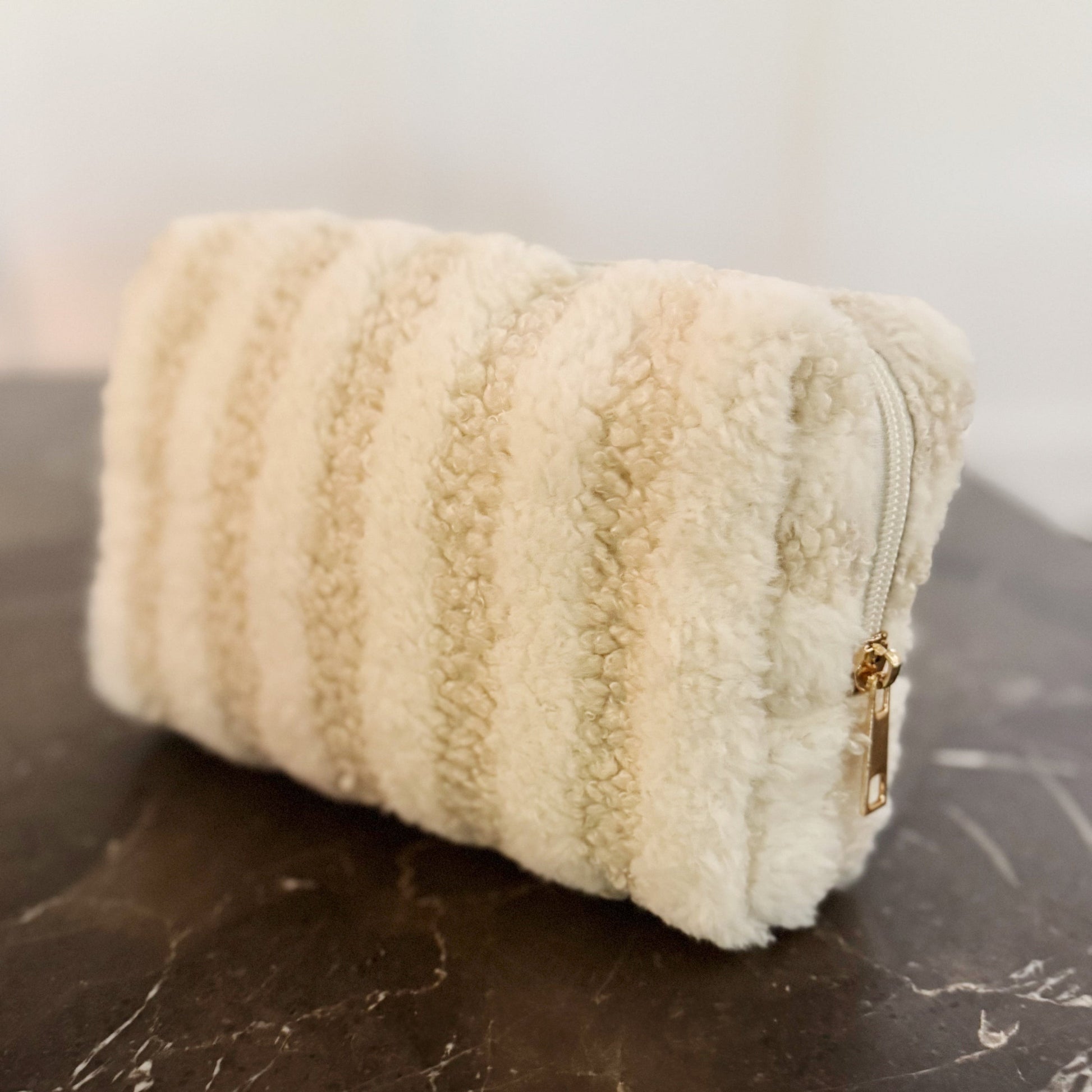 Beige textured pouch with a gold zipper on a dark surface