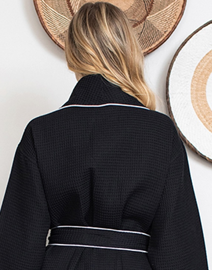 Person wearing a black Waffle Kimono Knee-Length robe with white trim, standing against a wall with decorative plates.