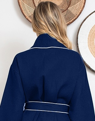 Person wearing a navy blue Waffle Kimono Knee-Length robe with white trim, standing in front of decorative wall items.
