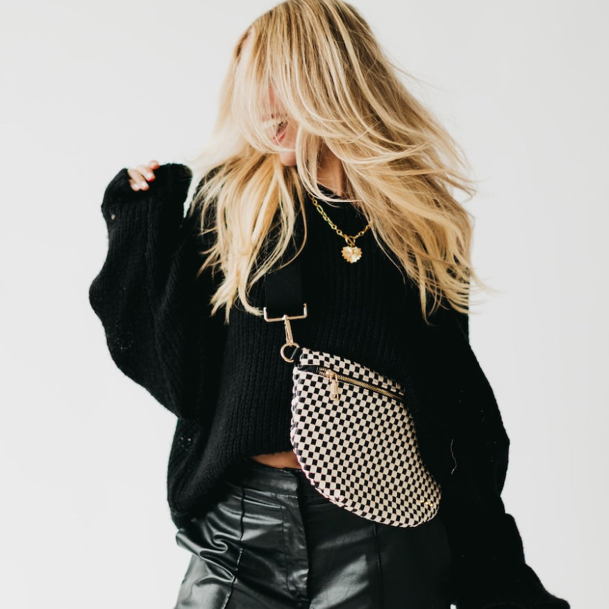 Person wearing a black sweater and holding a checkered handbag against a white background