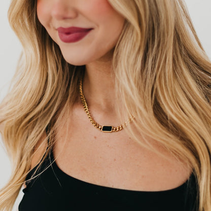 Close-up of a person wearing a gold chain necklace with a black pendant.