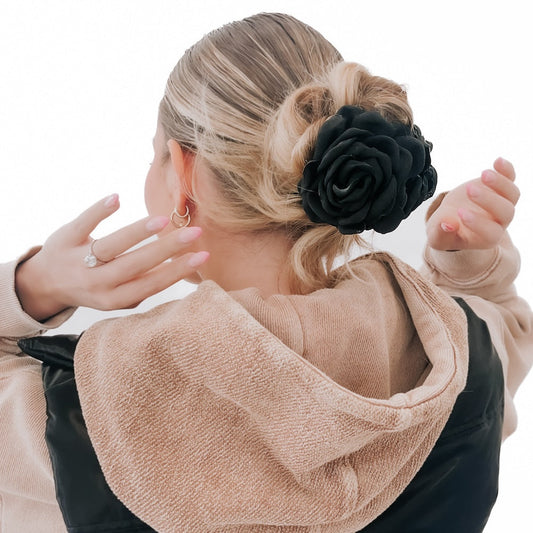 Woman with a black flower hair clip wearing a beige jacket on a white background
