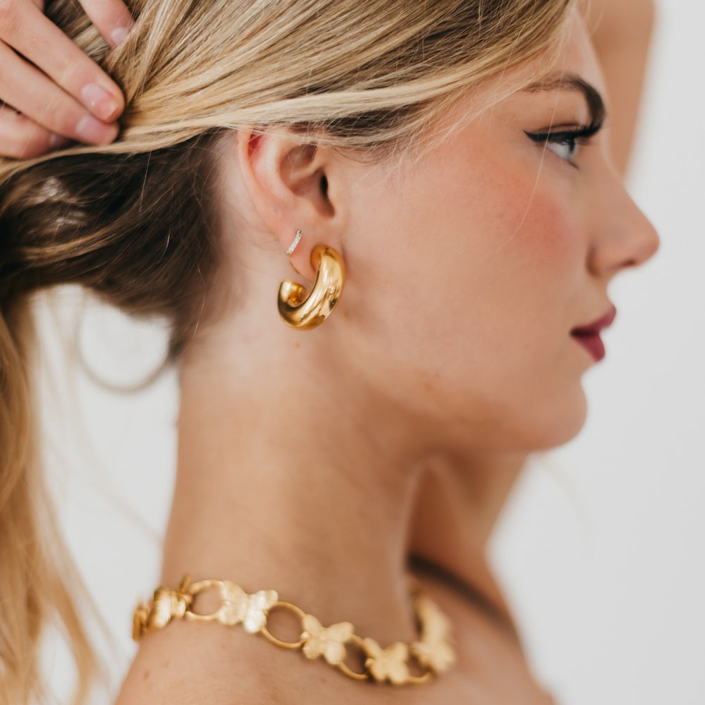 Woman wearing gold hoop earrings and bracelet with a neutral background