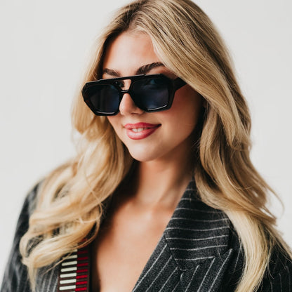 Woman wearing sunglasses and a striped blazer against a plain background