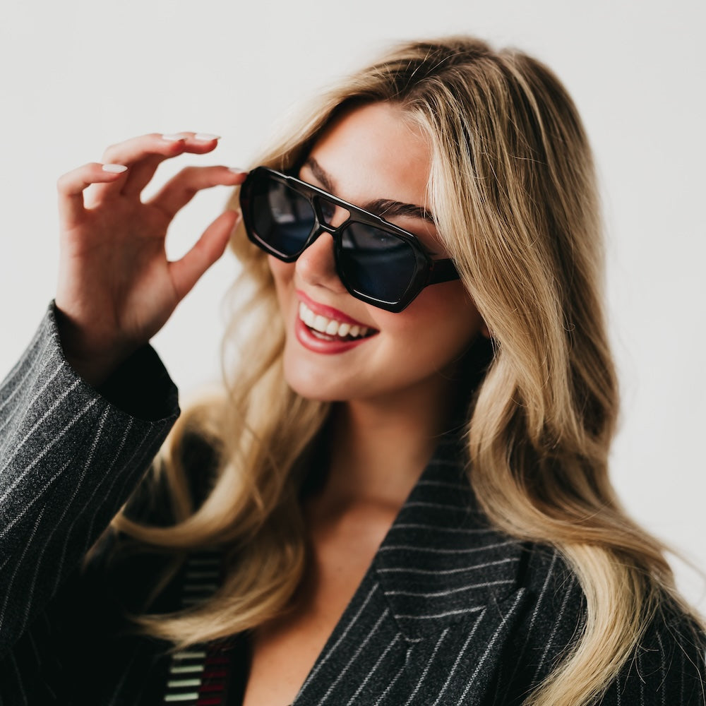 Woman wearing sunglasses and a pinstripe jacket against a neutral background