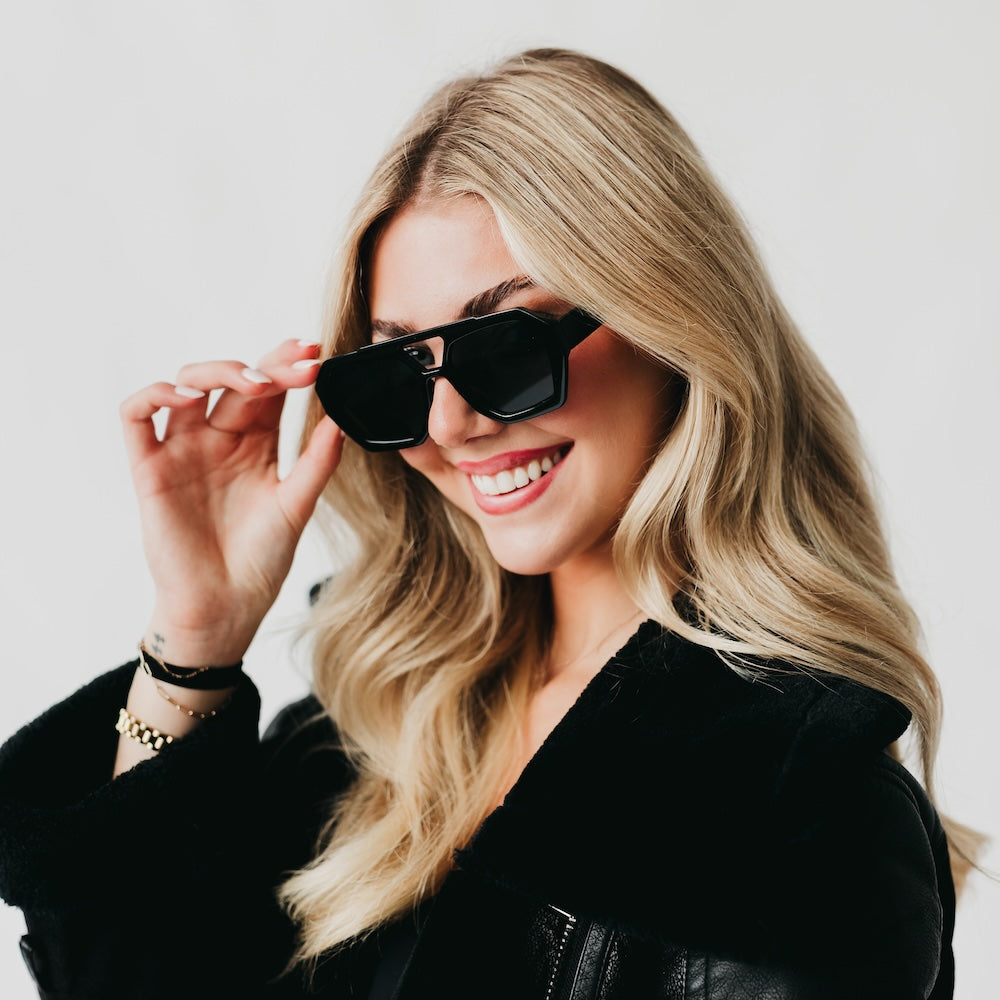 Woman wearing black sunglasses and a black leather jacket against a light background