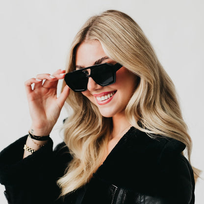 Woman wearing black sunglasses and a black leather jacket against a light background