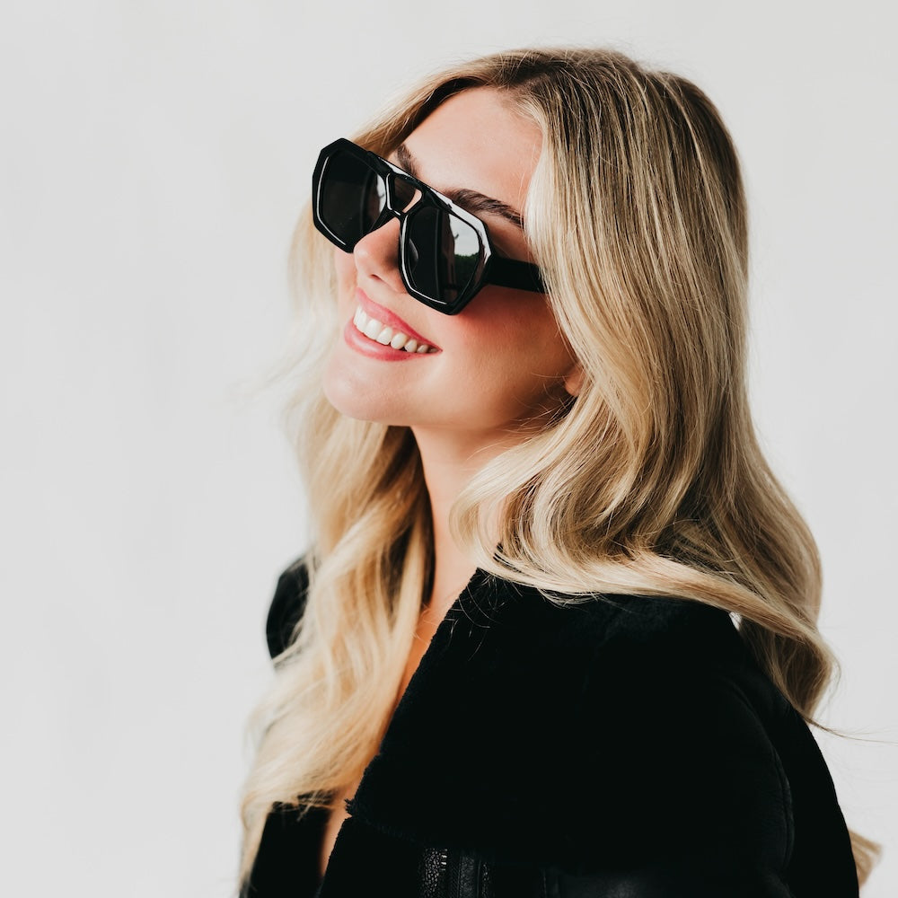 Woman wearing black sunglasses and a black outfit against a light background