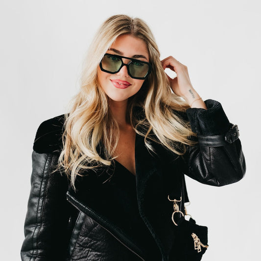 Woman wearing a black leather jacket and sunglasses on a plain background