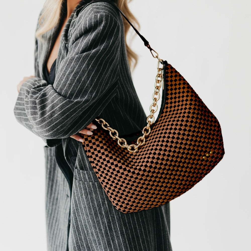 Person holding a woven handbag with a gold chain strap on a plain background