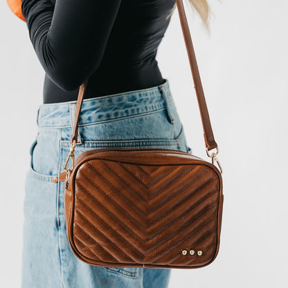 Brown chevron-patterned crossbody bag worn by a person with a plain background