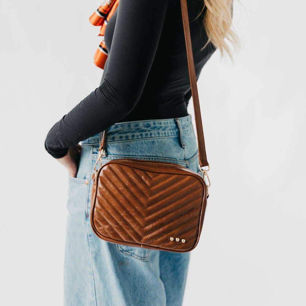 Person wearing a brown quilted crossbody bag on a plain background