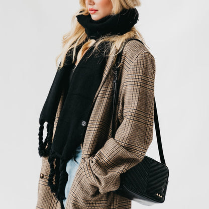 Woman wearing a plaid coat and black scarf, holding a black handbag on a white background