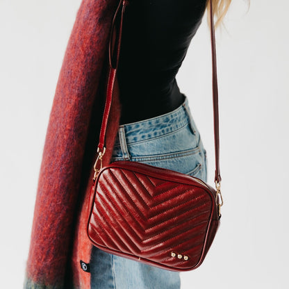 Red quilted handbag with gold accents held by a person wearing a black top and blue jeans.