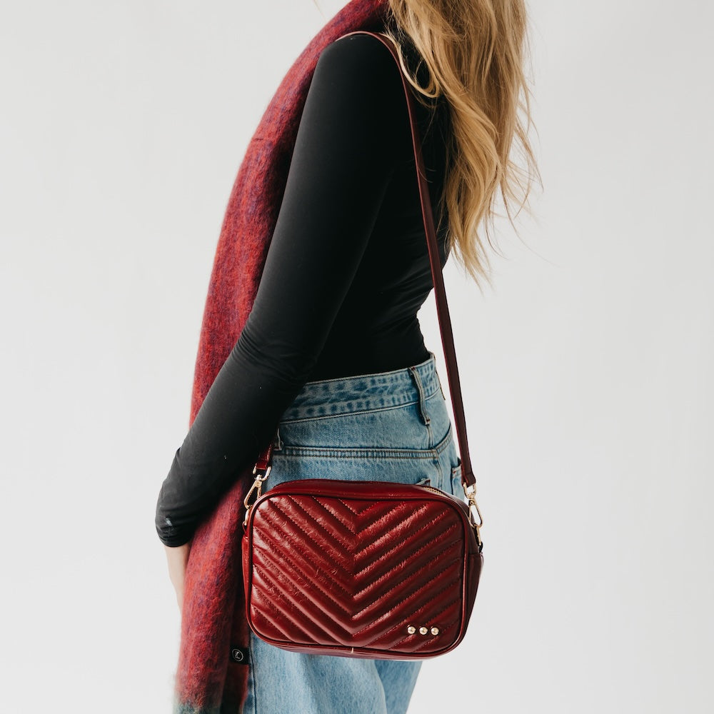 Person wearing a red quilted handbag with a plain background