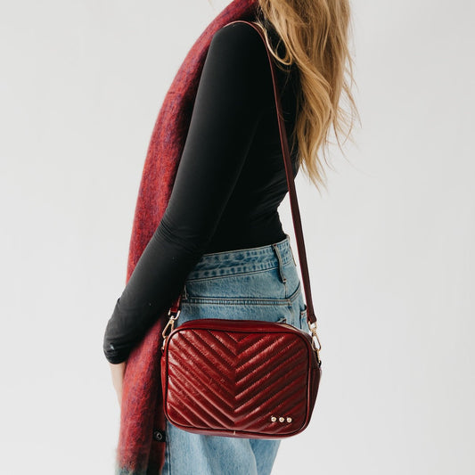 Person wearing a red quilted handbag with a plain background