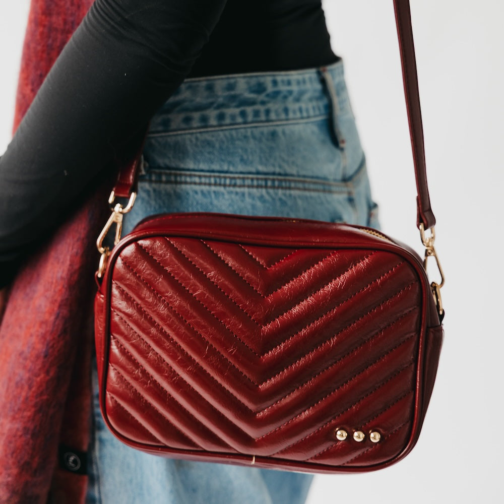Red textured handbag with gold accents held by a person wearing jeans and a black top.