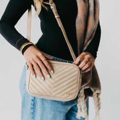 Person holding a beige quilted handbag with a neutral background