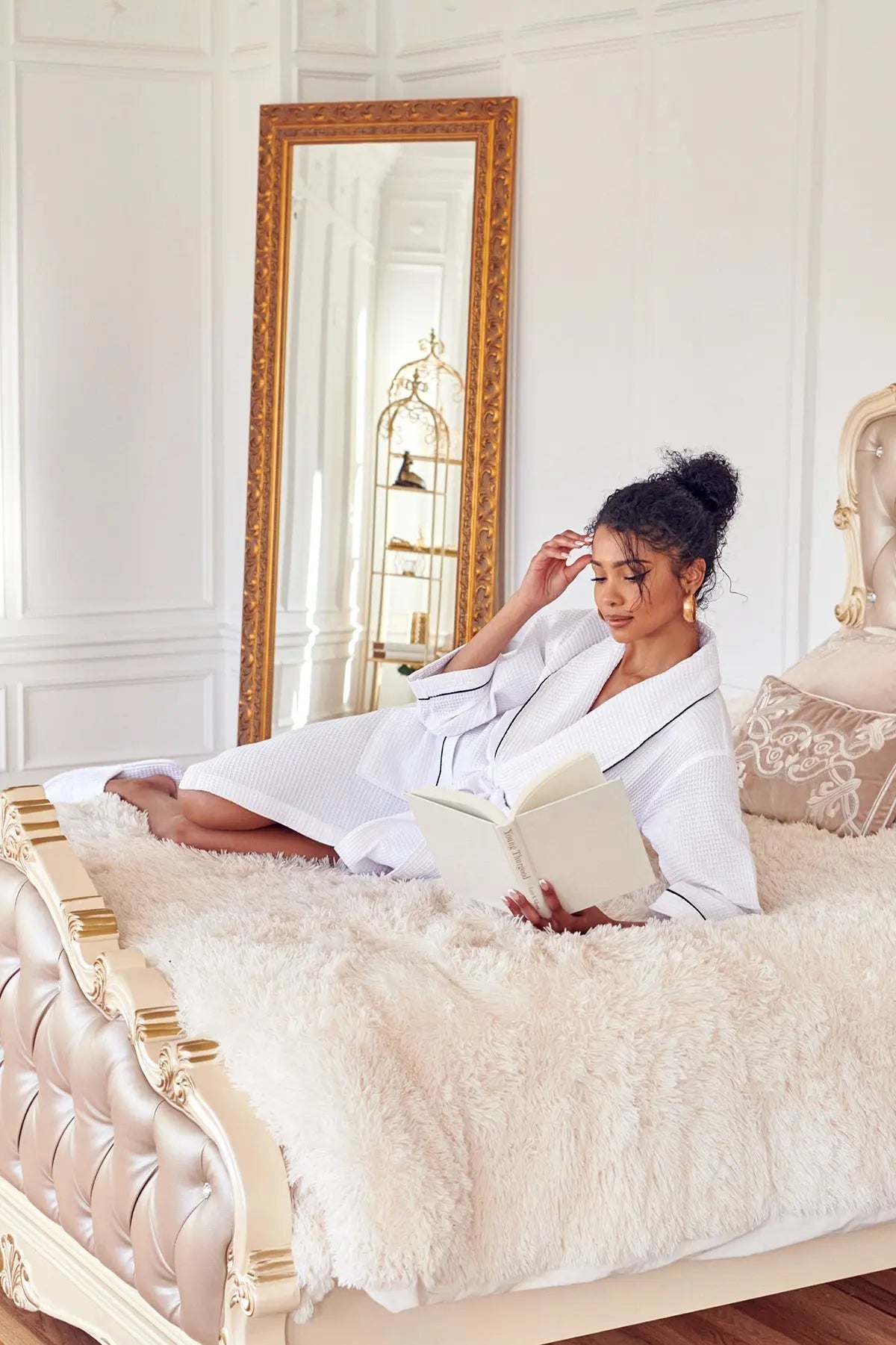 Woman in white Waffle Kimono Robe Knee-Length robe reading a book on a plush bed in a stylish bedroom.