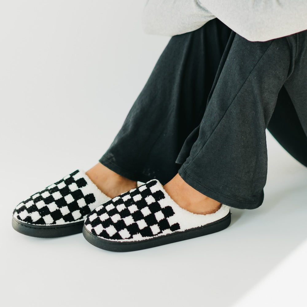 Black and white checkered slippers worn with dark pants on a light background