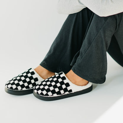 Black and white checkered slippers worn with dark pants on a light background