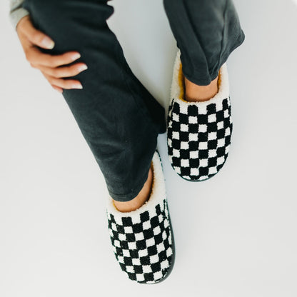 Black and white checkered slippers worn with black pants on a light background