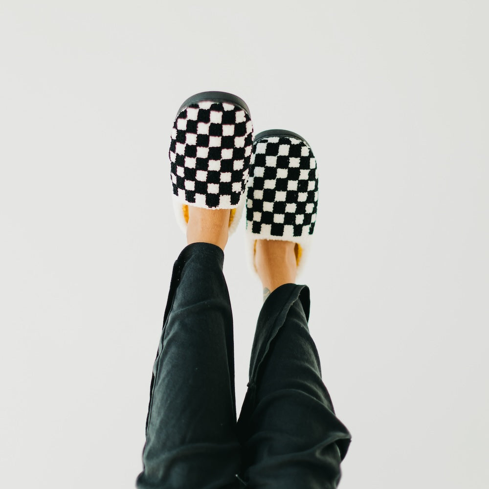Checkered slippers worn with black pants on a light gray background