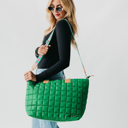 Woman holding a green quilted handbag against a plain background