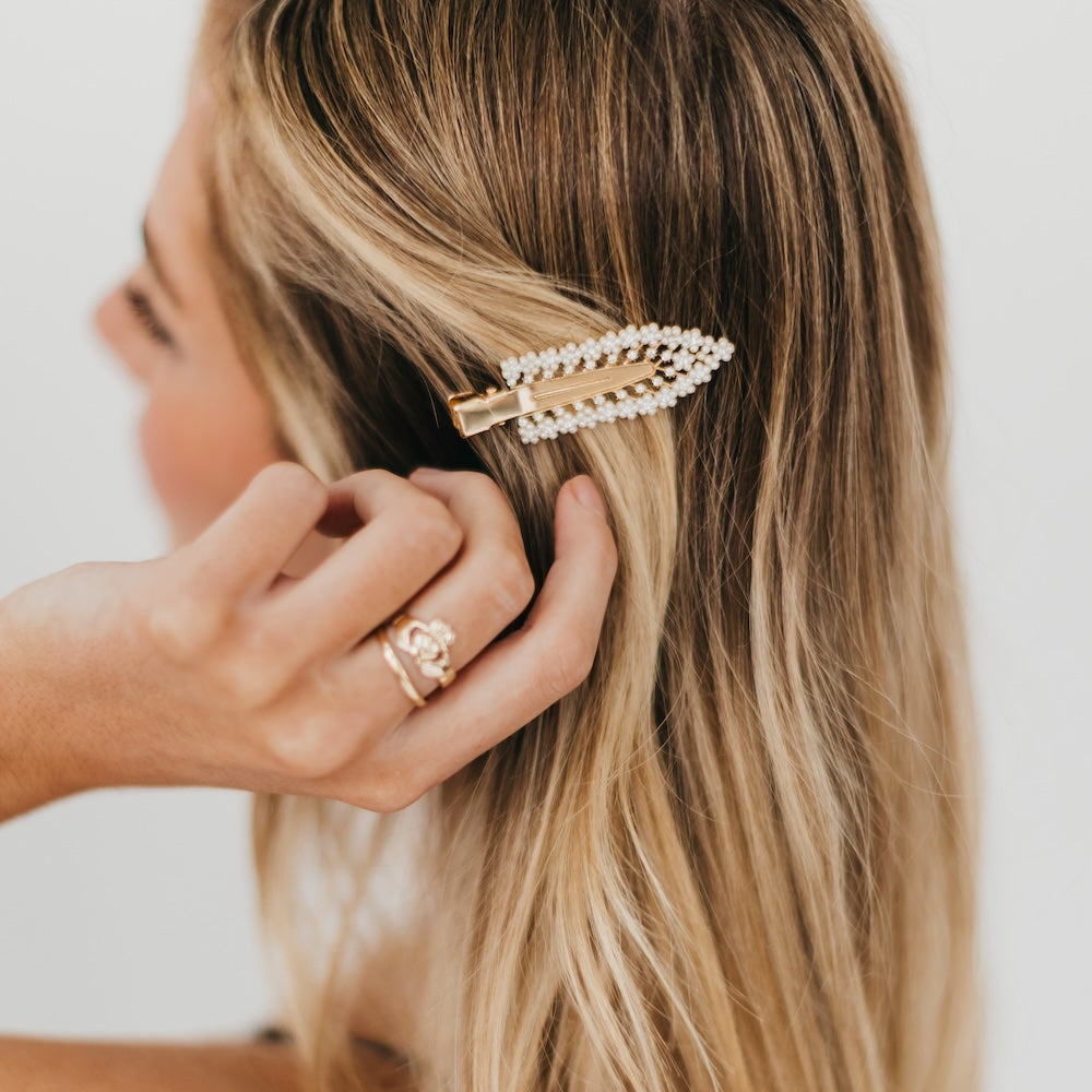 Woman adjusting a decorative diamond and pearl hair clip with pearls in her blonde hair.
