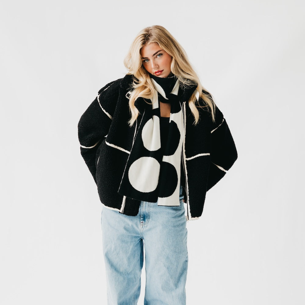 Woman wearing a black and white patterned jacket with light blue jeans on a white background