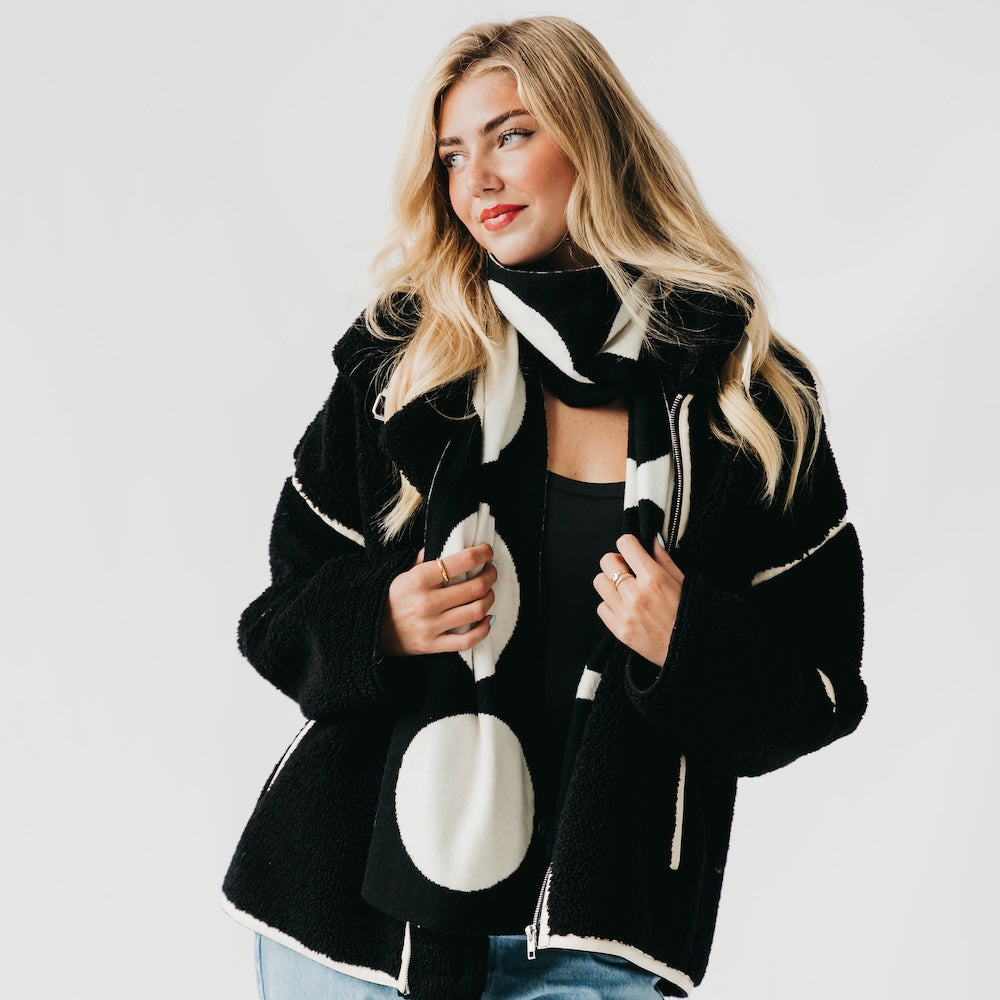 Woman wearing a black and white circle patterned coat on a plain background