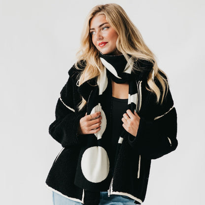 Woman wearing a black and white circle patterned coat on a plain background