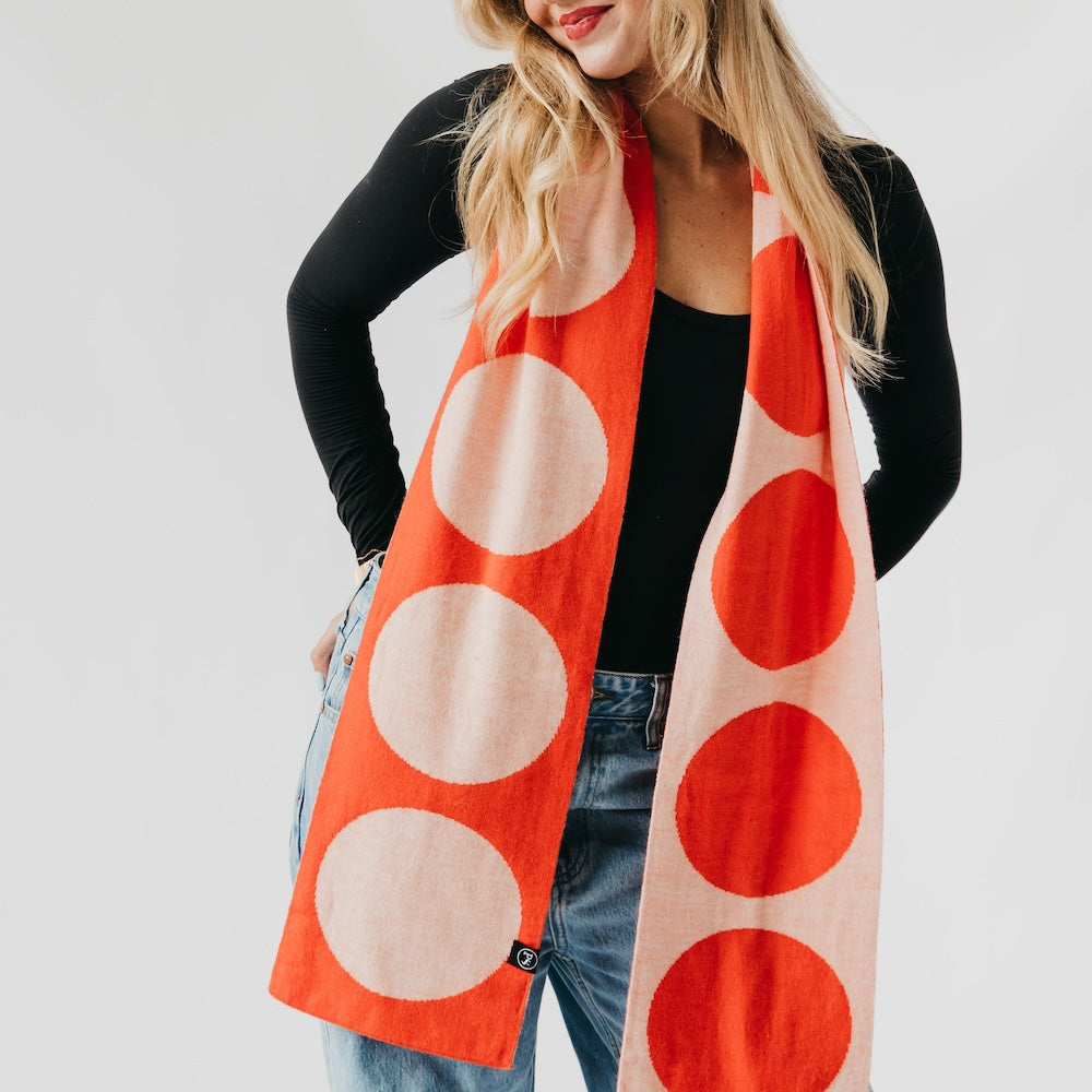 Woman wearing a long orange scarf with white circles on a plain background