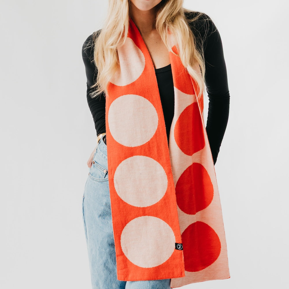 Person wearing a large orange scarf with red and beige circles on a plain background