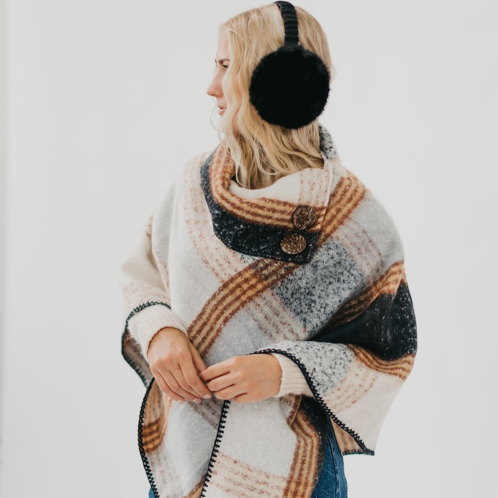 Person wearing a patterned poncho and black earmuffs on a white background