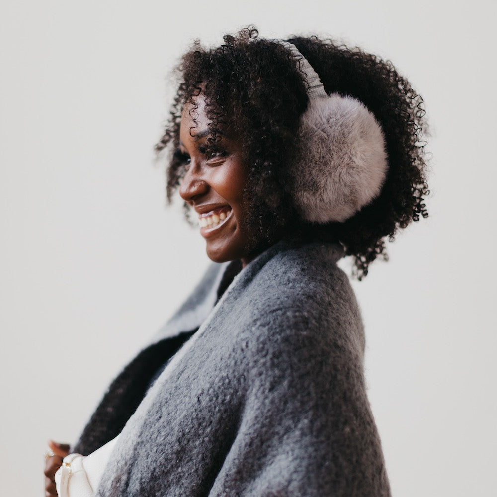 Woman wearing gray coat and white ear muffs against a light background