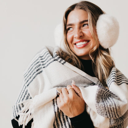 Woman wearing a plaid blanket, smiling, with a neutral background
