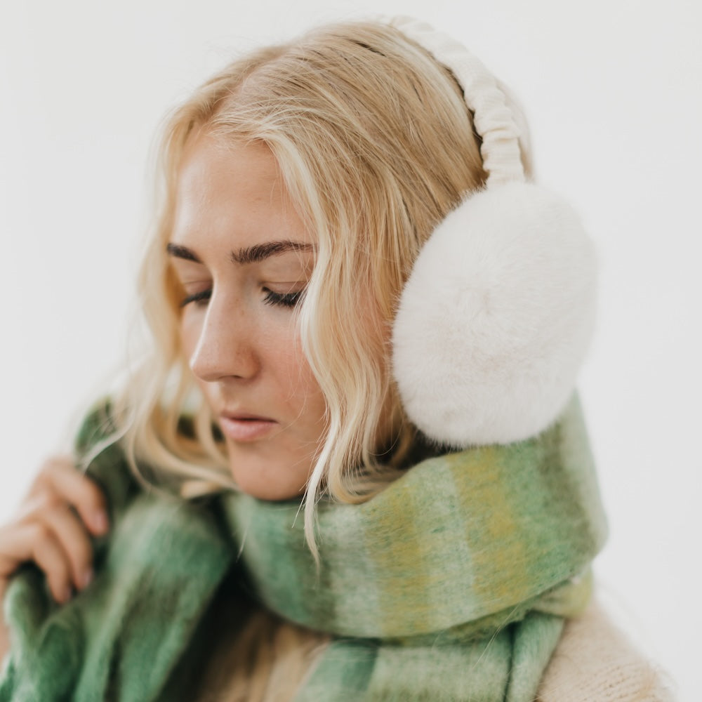 Woman wearing white earmuffs and a green scarf against a white background