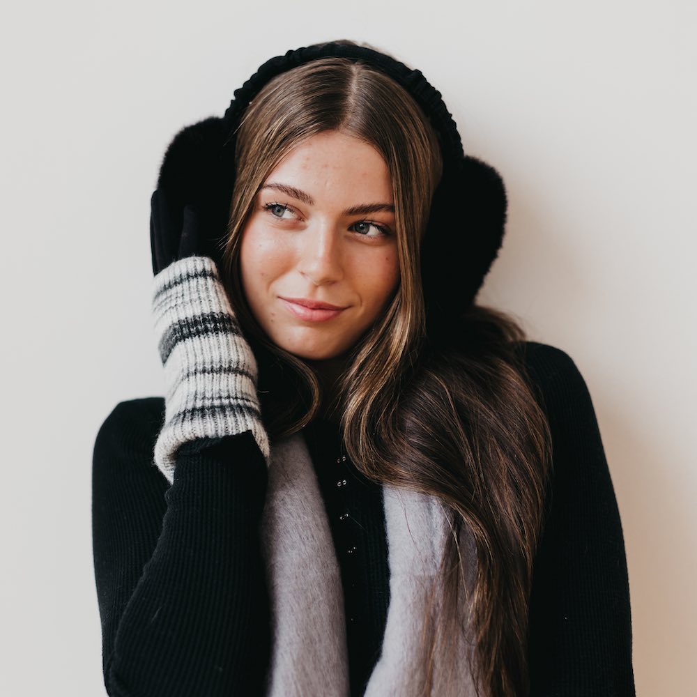 Woman wearing a black coat, scarf, gloves, and earmuffs against a white background