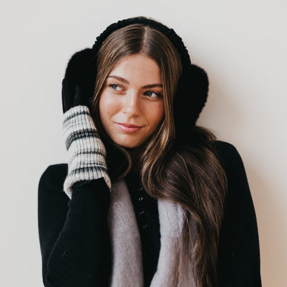 Woman wearing a black coat, scarf, gloves, and earmuffs against a white background