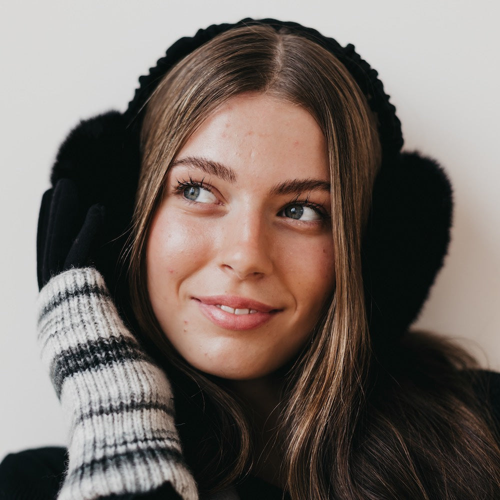 Woman wearing black earmuffs and a striped glove against a neutral background